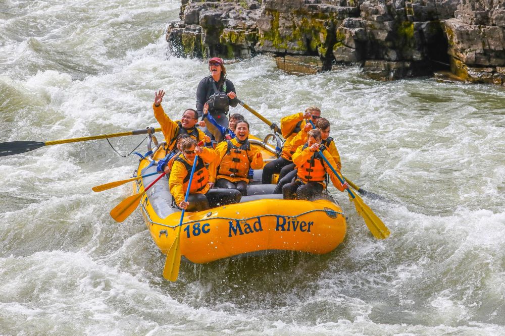 Group whitewater rafting in a yellow raft on a river.