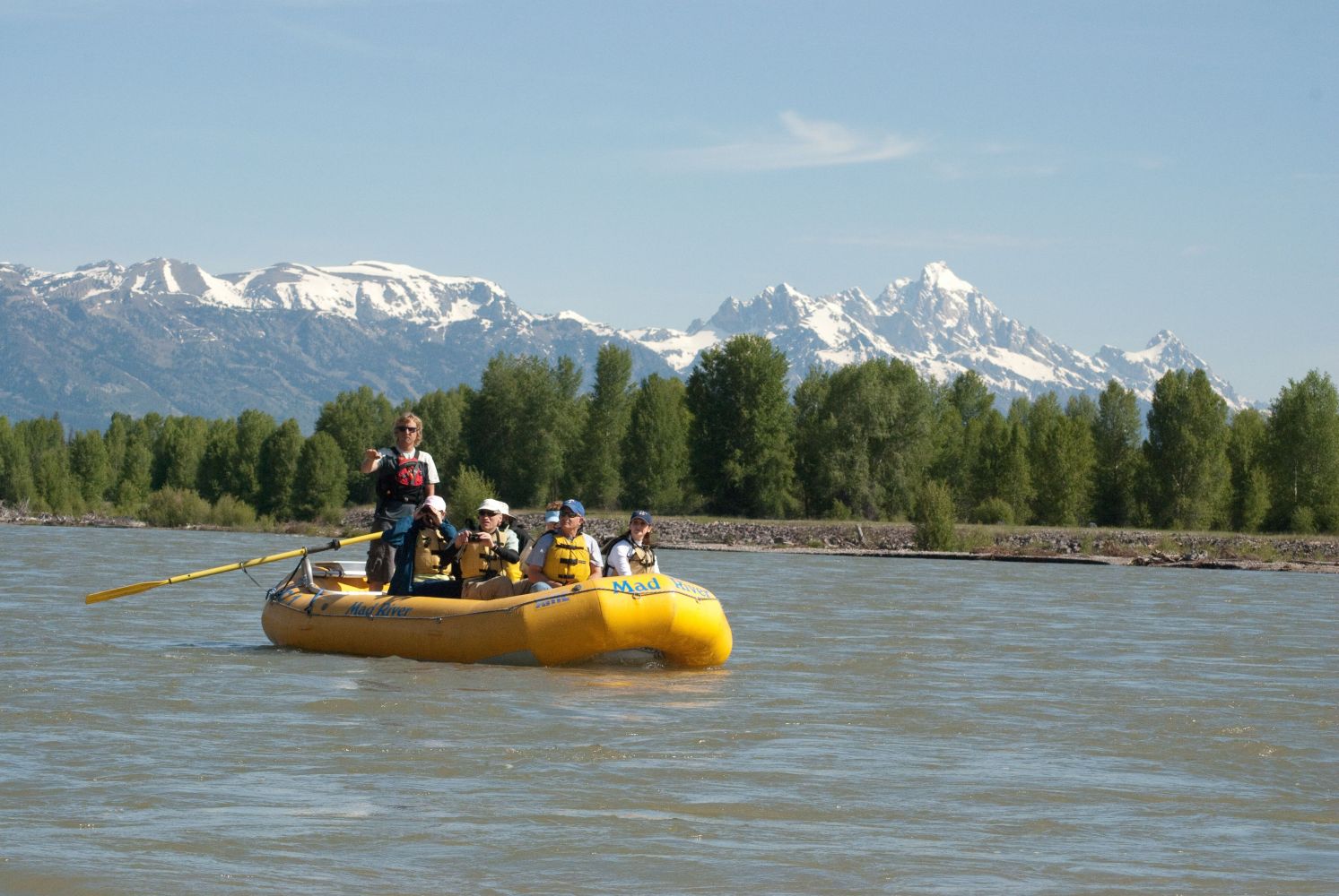 People rafting on a river with snow-capped mountains in the background.