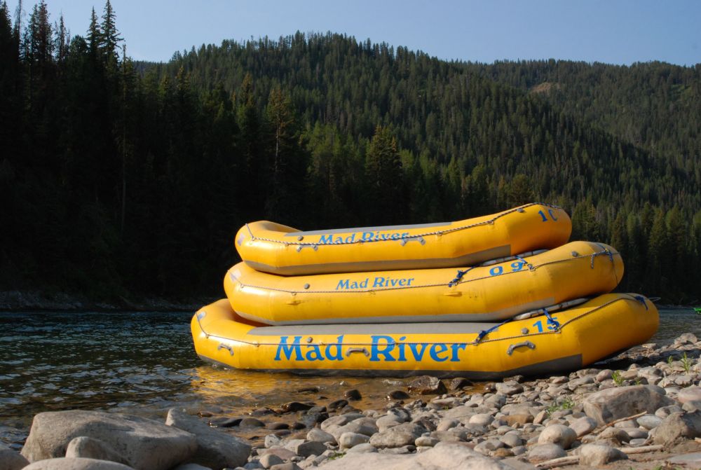Stacked yellow rafts by a rocky riverbank with forested hills.